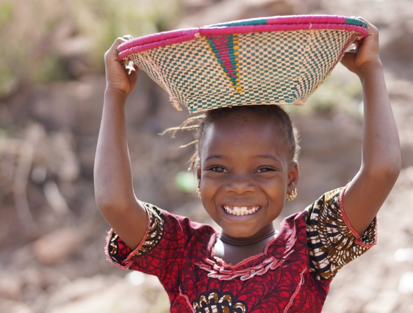 Smiling African Ethnic Girl Outdoors with Food Basket, poverty symbol